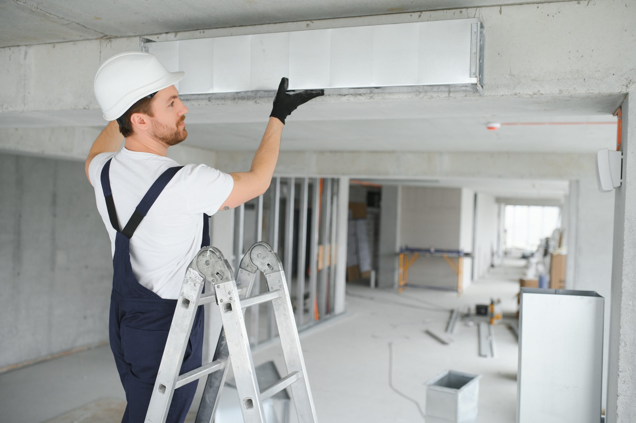 Professional HVAC Worker on a Aluminium Scaffolding Installing Air Duct Inside Newly Built Commercial Building. Industrial Theme.