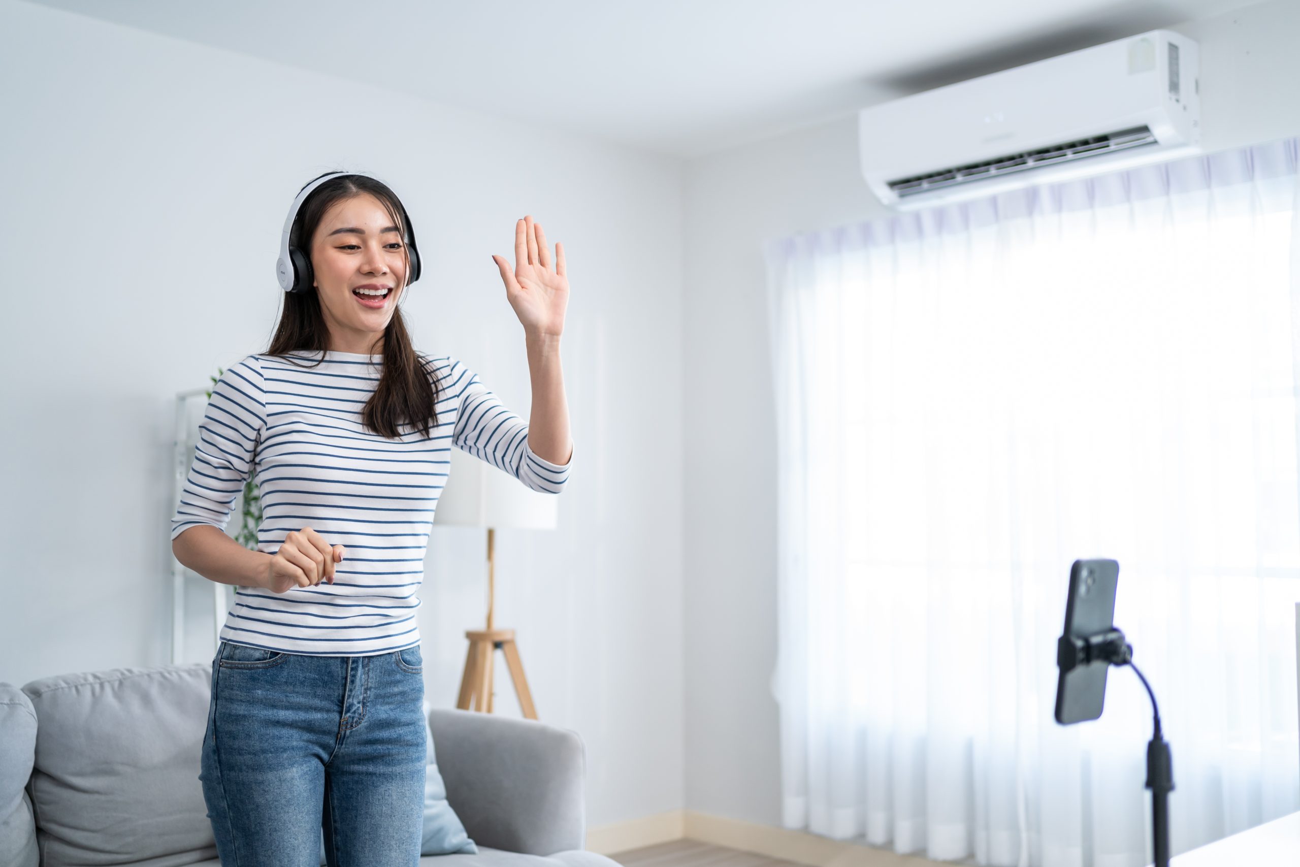 Asian attractive woman enjoy dance with music in living room at home. Beautiful female use mobile phone recording challenge video virtual clip sing a song, enjoy weekend activity lifestyles in house.