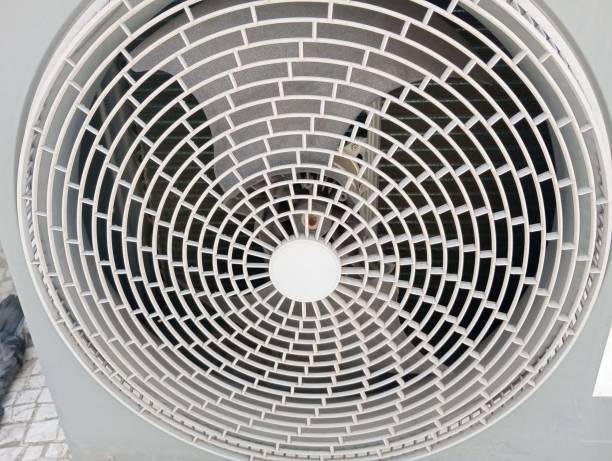 A close-up front view of a circular white plastic fan grille of an outdoor air conditioning unit showing a concentric grid pattern with the fan blades visible inside.